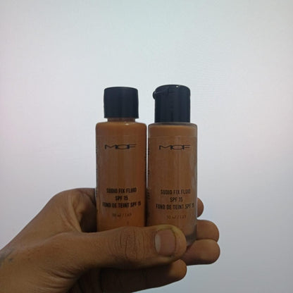 Two bottles of MGF Studio Fix Fluid SPF 15 held in a hand against a white background