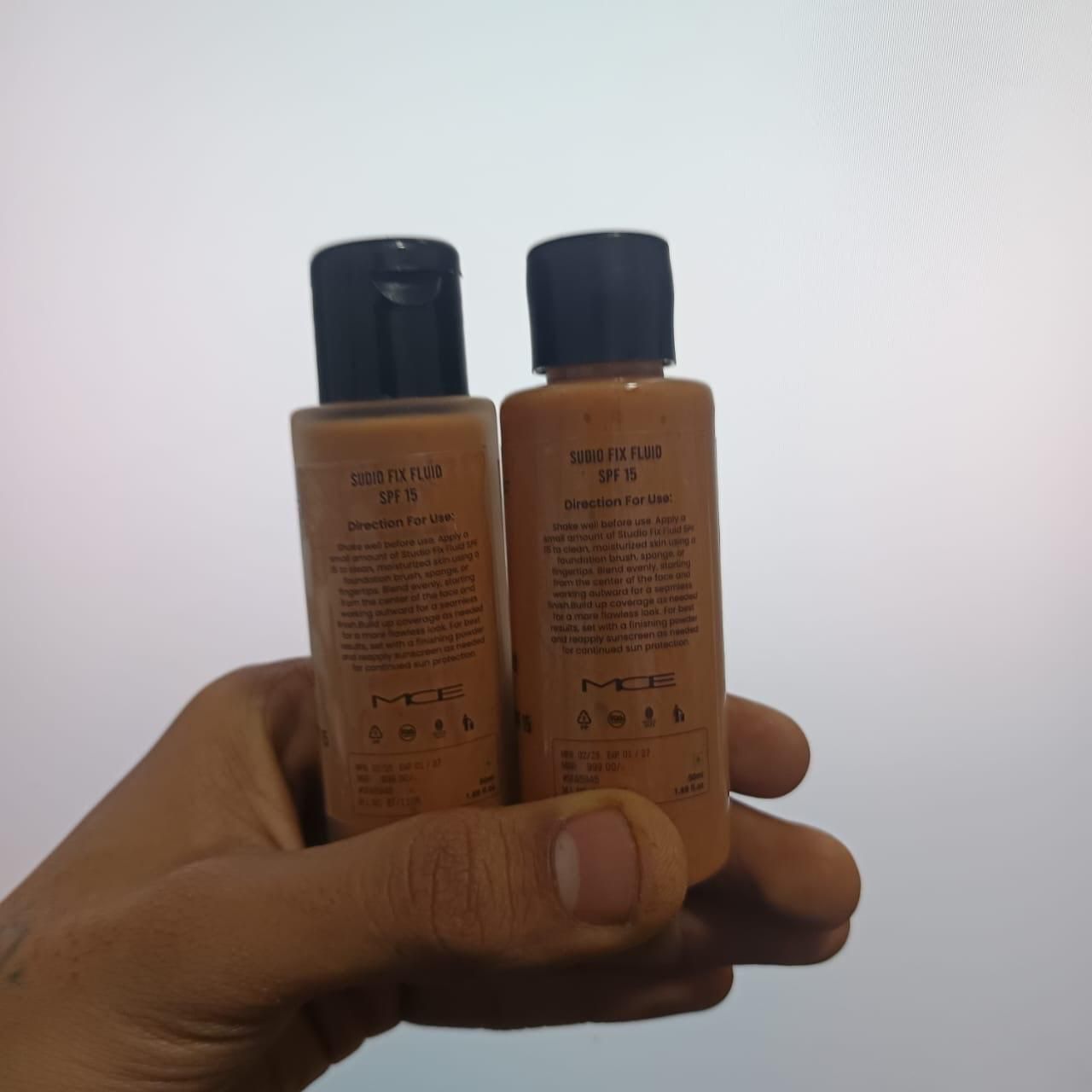 Two bottles of MCE sun screen fluid held in a hand against a white background